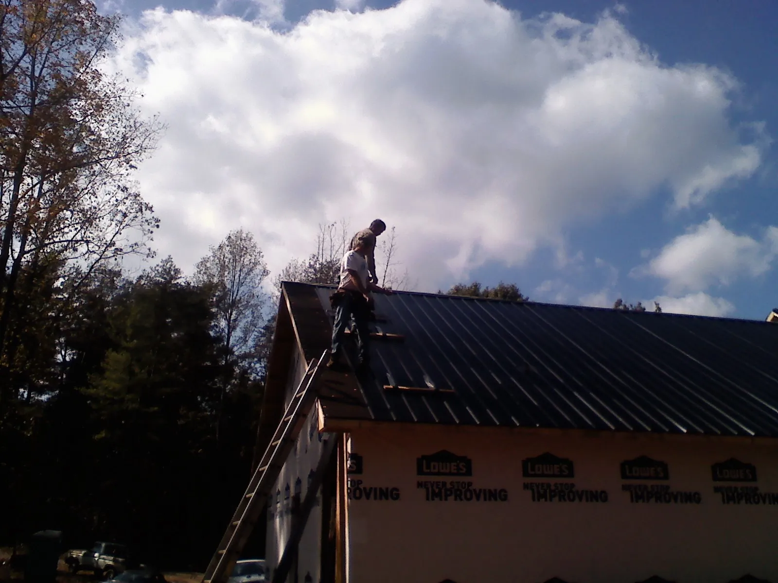 Roofer fastening dark metal panels high against a cloudy sky, from a Roof Inspection job in Lynnville