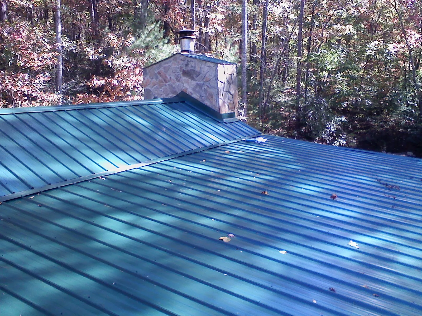 New green metal roof and stone chimney surrounded by autumn woods in Lynnville